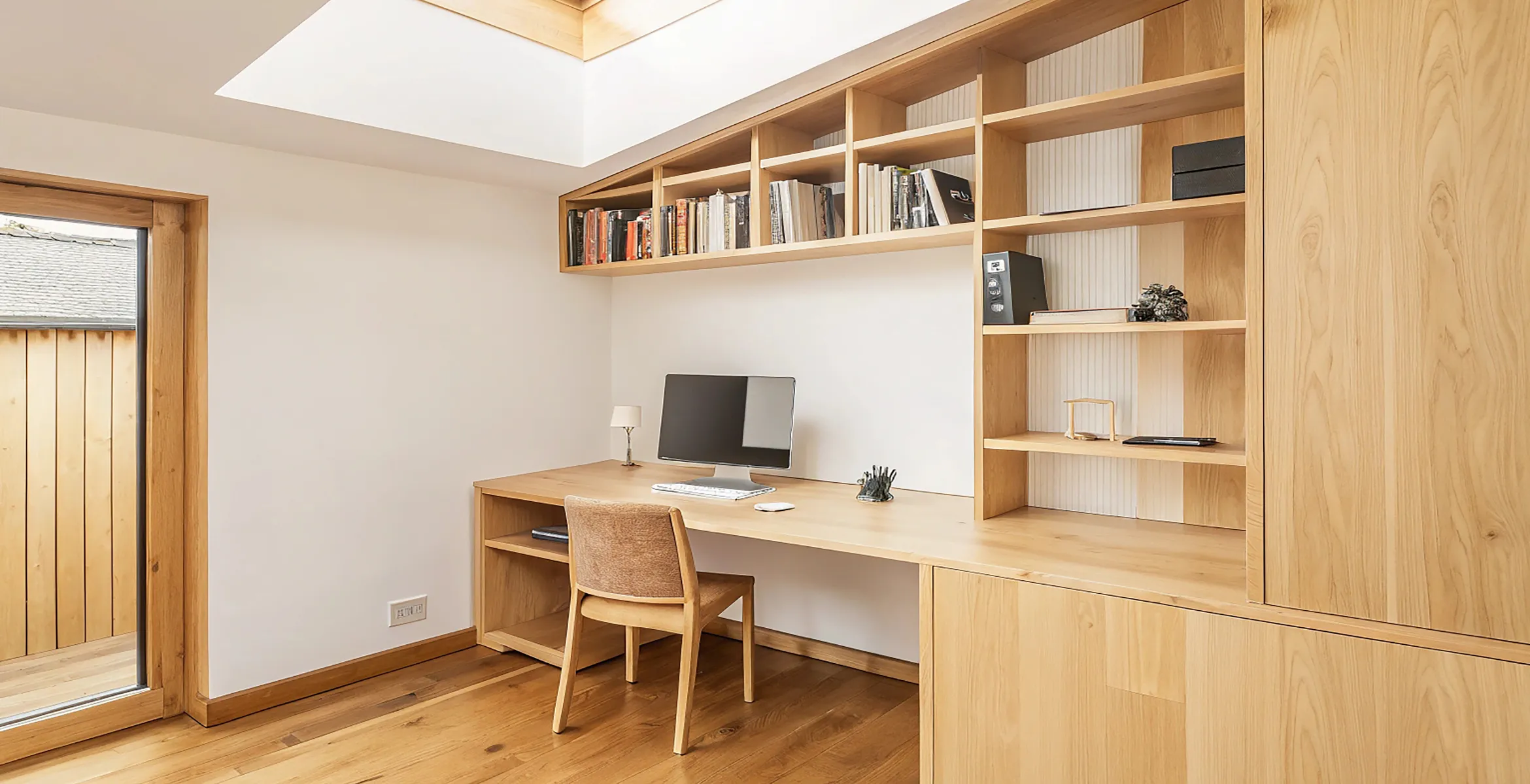 Dedicated home office addition in Dallas TX with floor-to-ceiling wood shelving, custom desk, skylight illumination, and a warm contemporary workspace layout